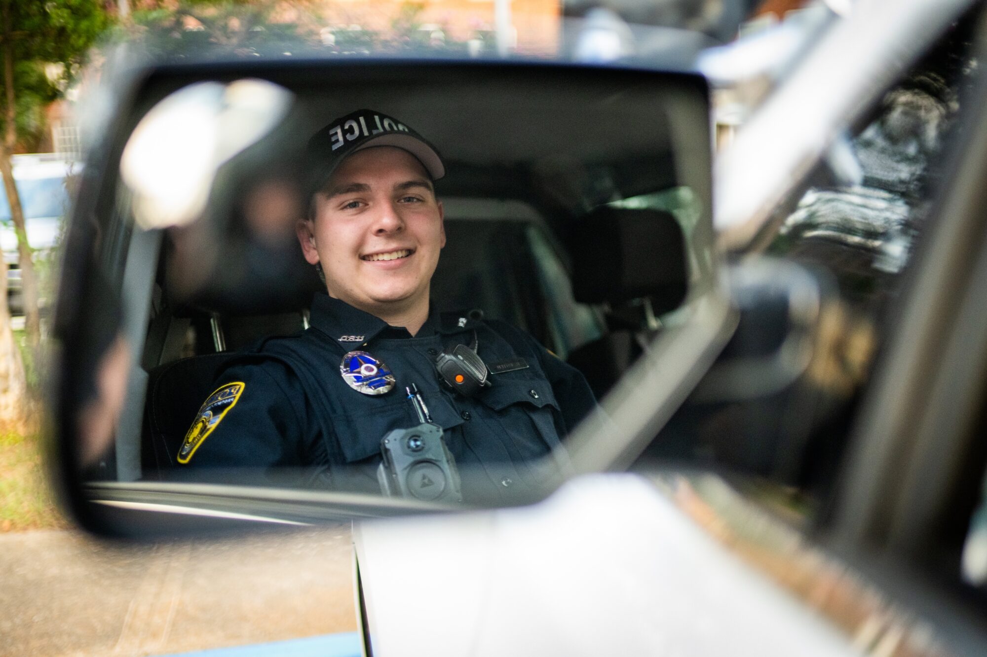 Police officer's smiling face is reflected in the police car's side mirror.