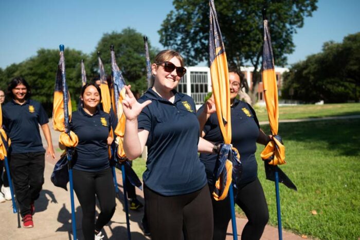 Decorative photo. Students hold blue and gold school flags and walk together.