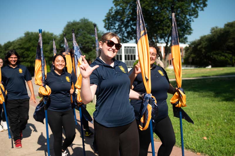 Decorative photo. Students hold blue and gold school flags and walk together.