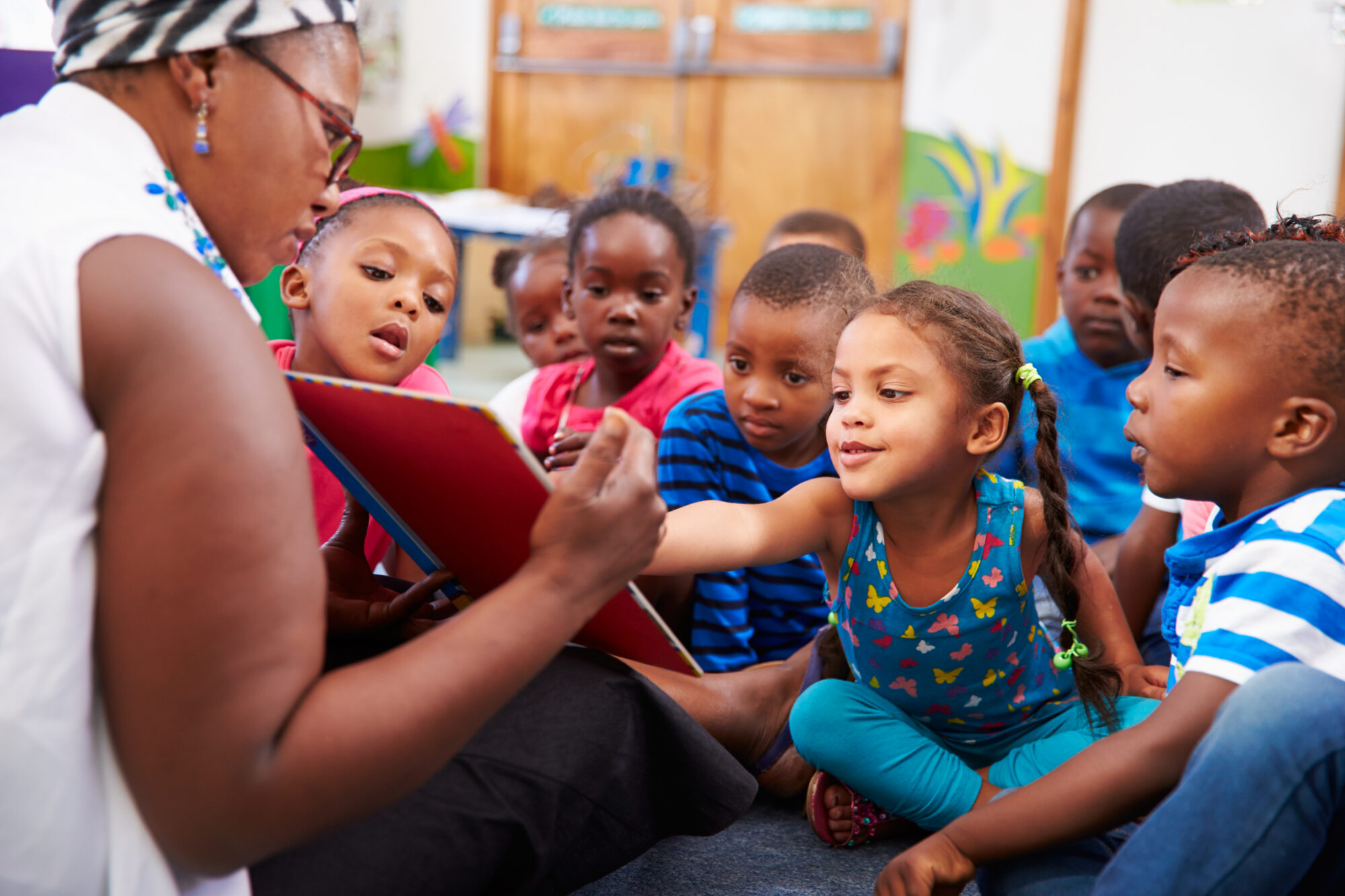 A group of young students reading a book with a teacher. 