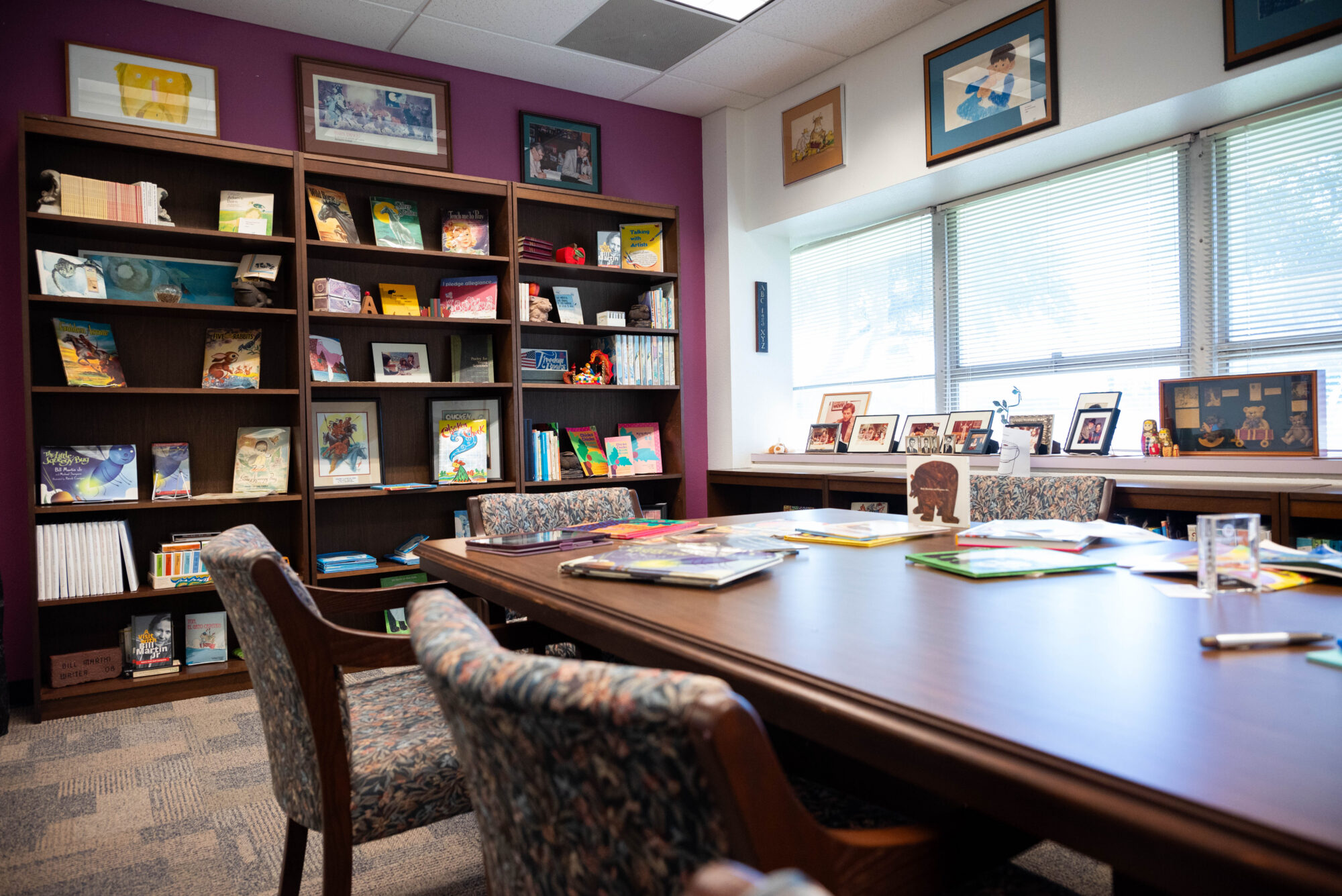 A table with children's books scattered across it, and a bookshelf full of books.