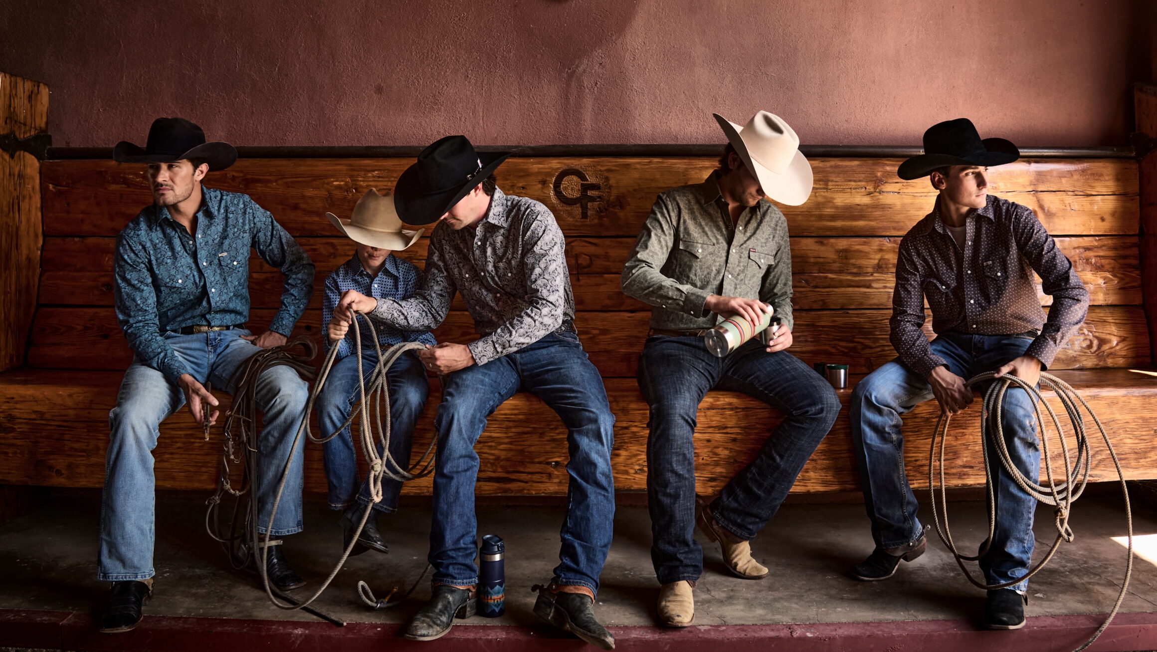 A group of people in western attire sitting on a wooden bench.