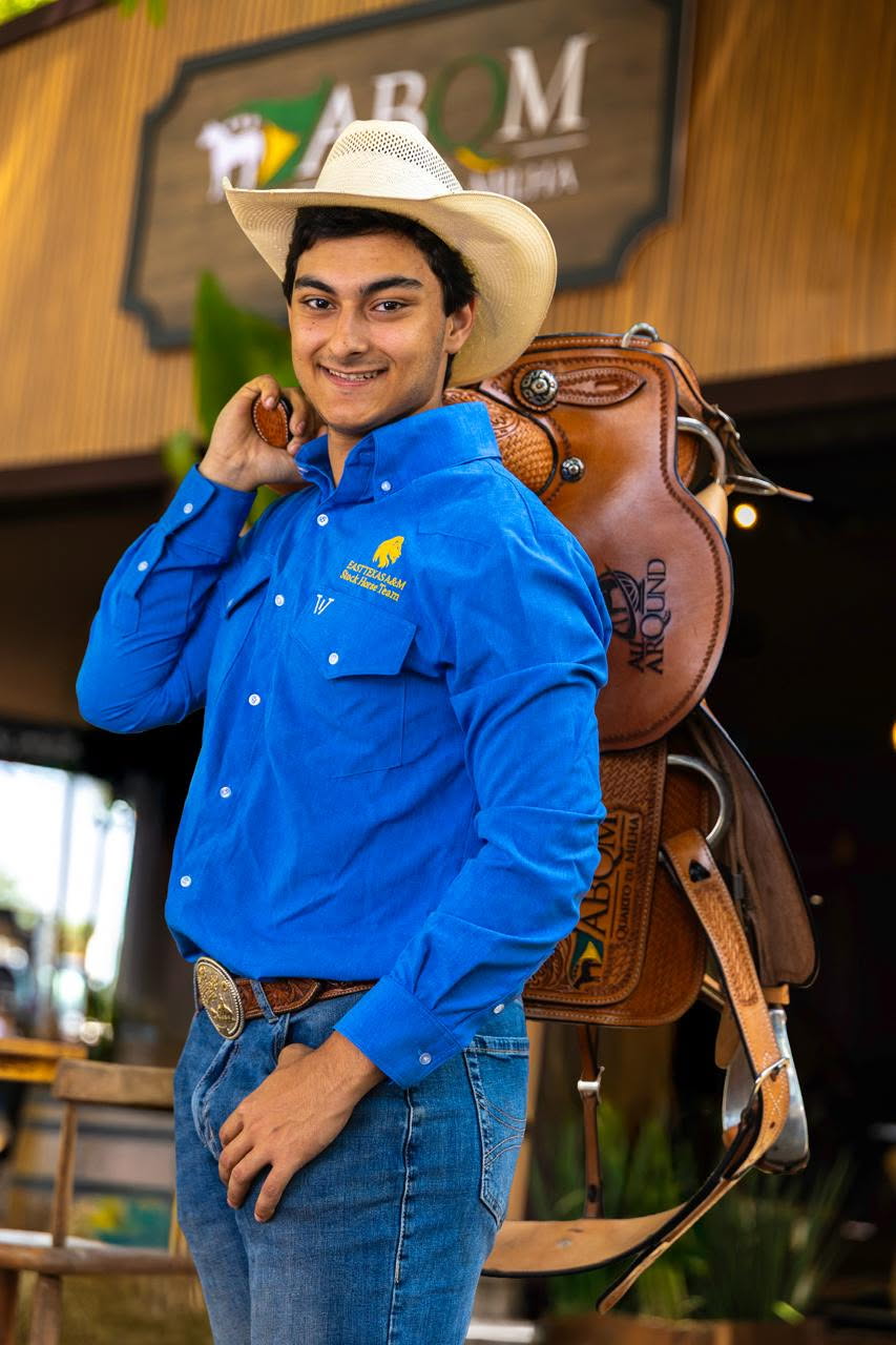 A person in western attire posing with a horse saddle.
