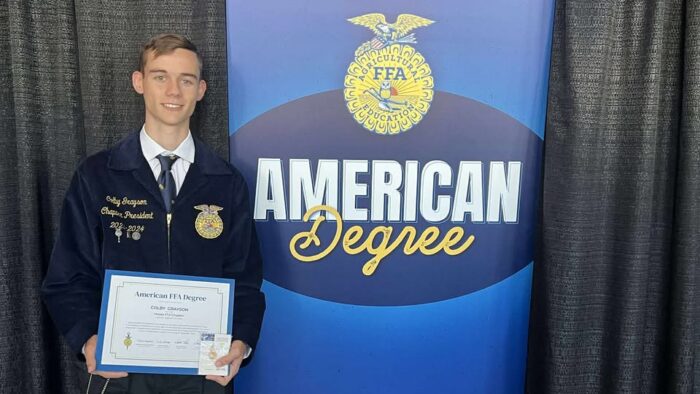 A person in a blue jacket posing with an award certificate.