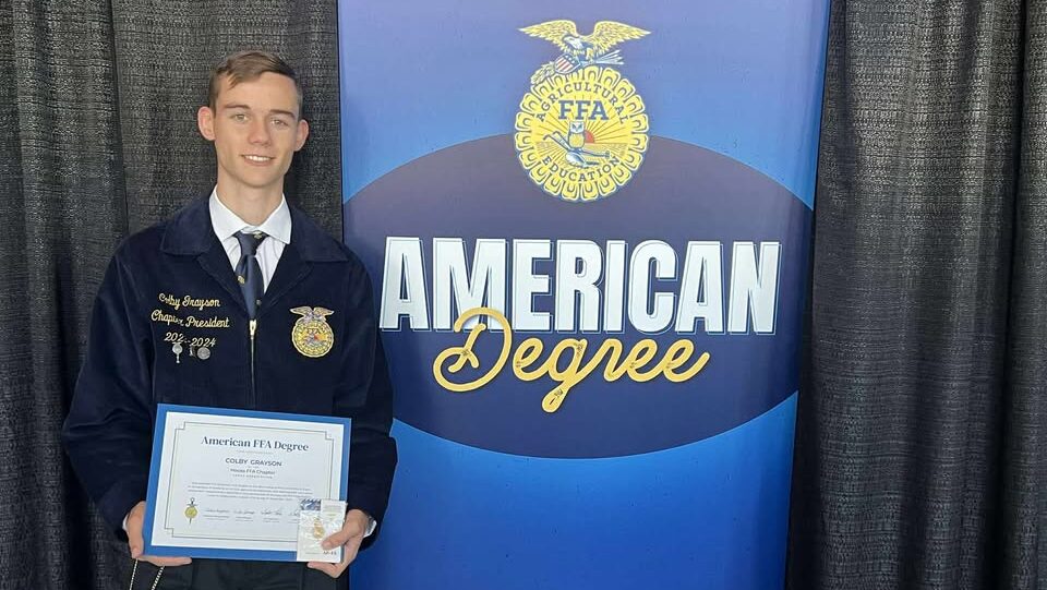 A person in a blue jacket posing with an award certificate.