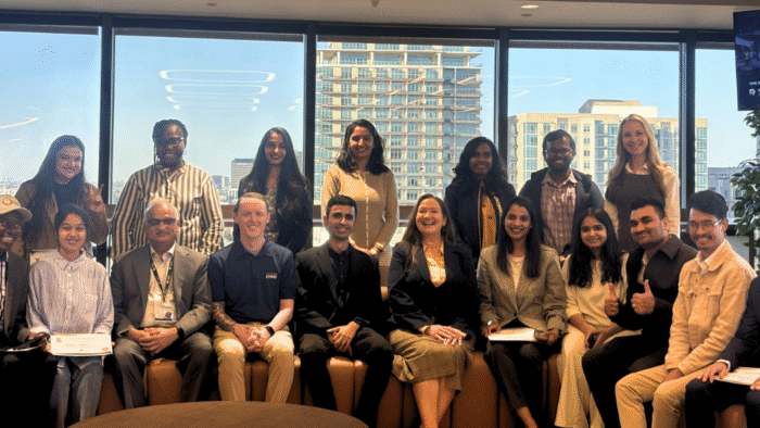 A group of students posing for a photo in front of a large window in a high rise building.