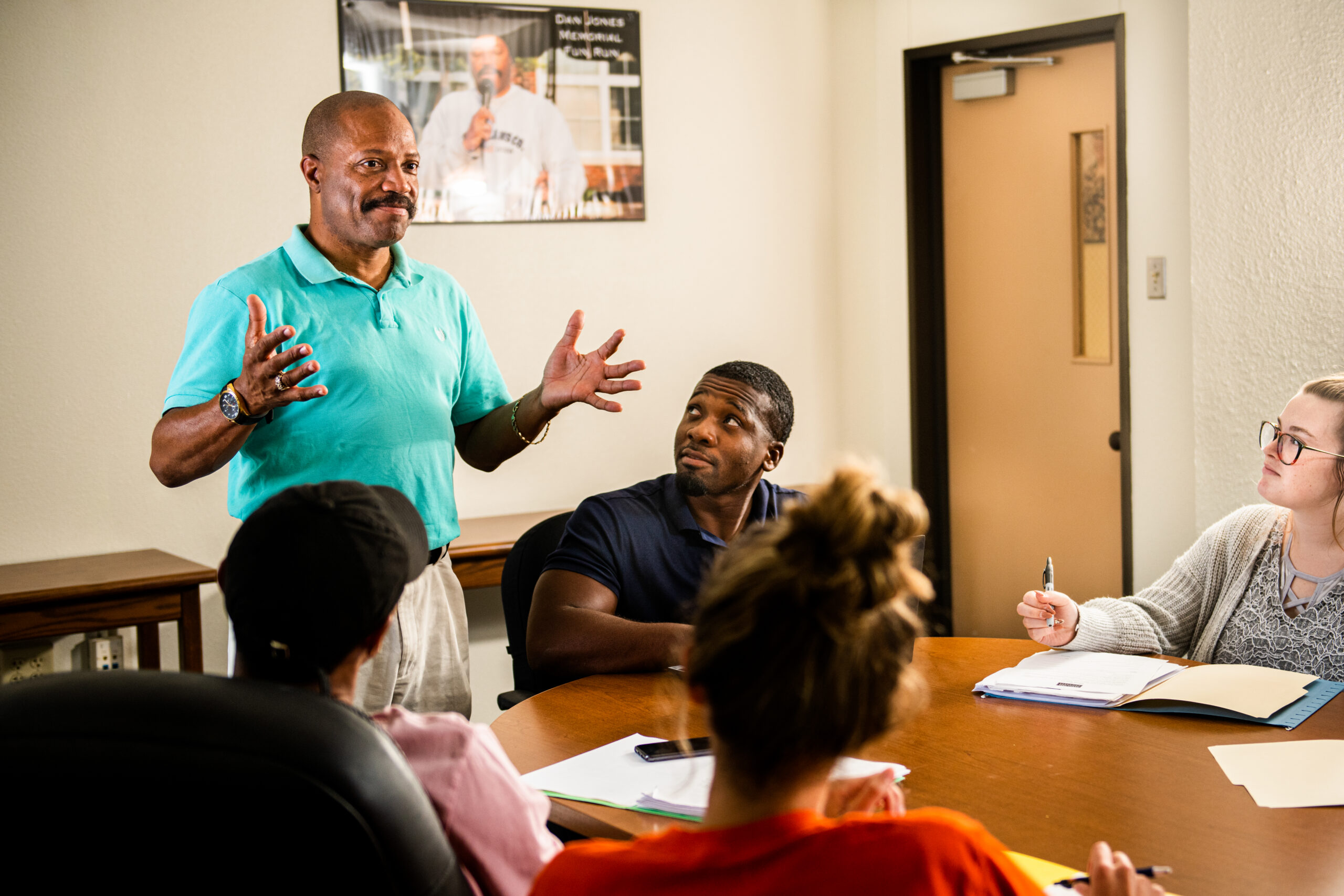 I man standing before a group of students seated at a table.