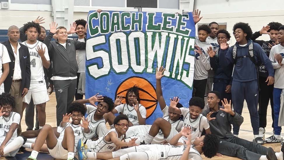 A large group of basket players is gathered around a sign reading "Coach Lee, 500 Wins".
