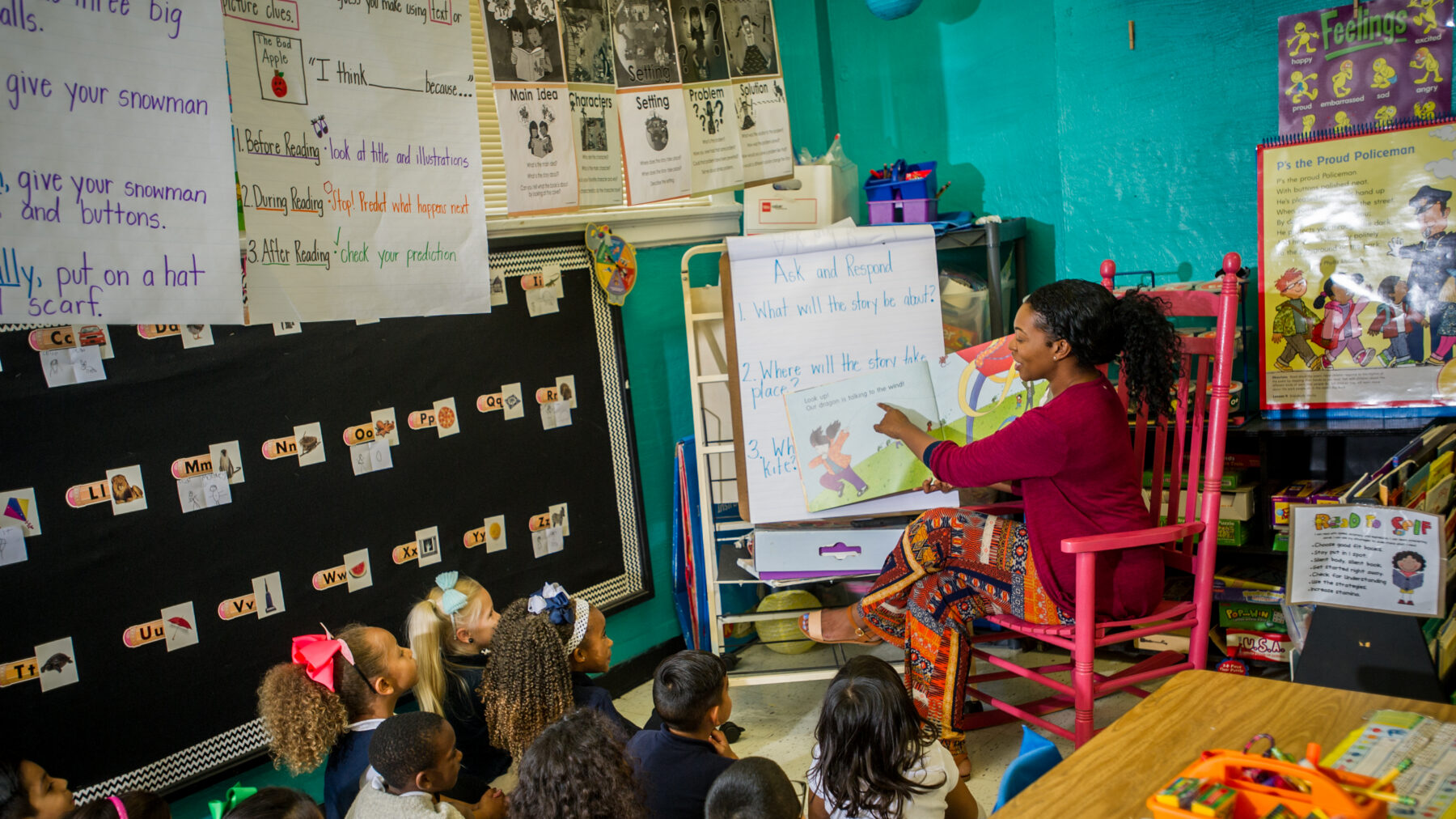 A woman teaching in a classroom with children sitting on the floor.