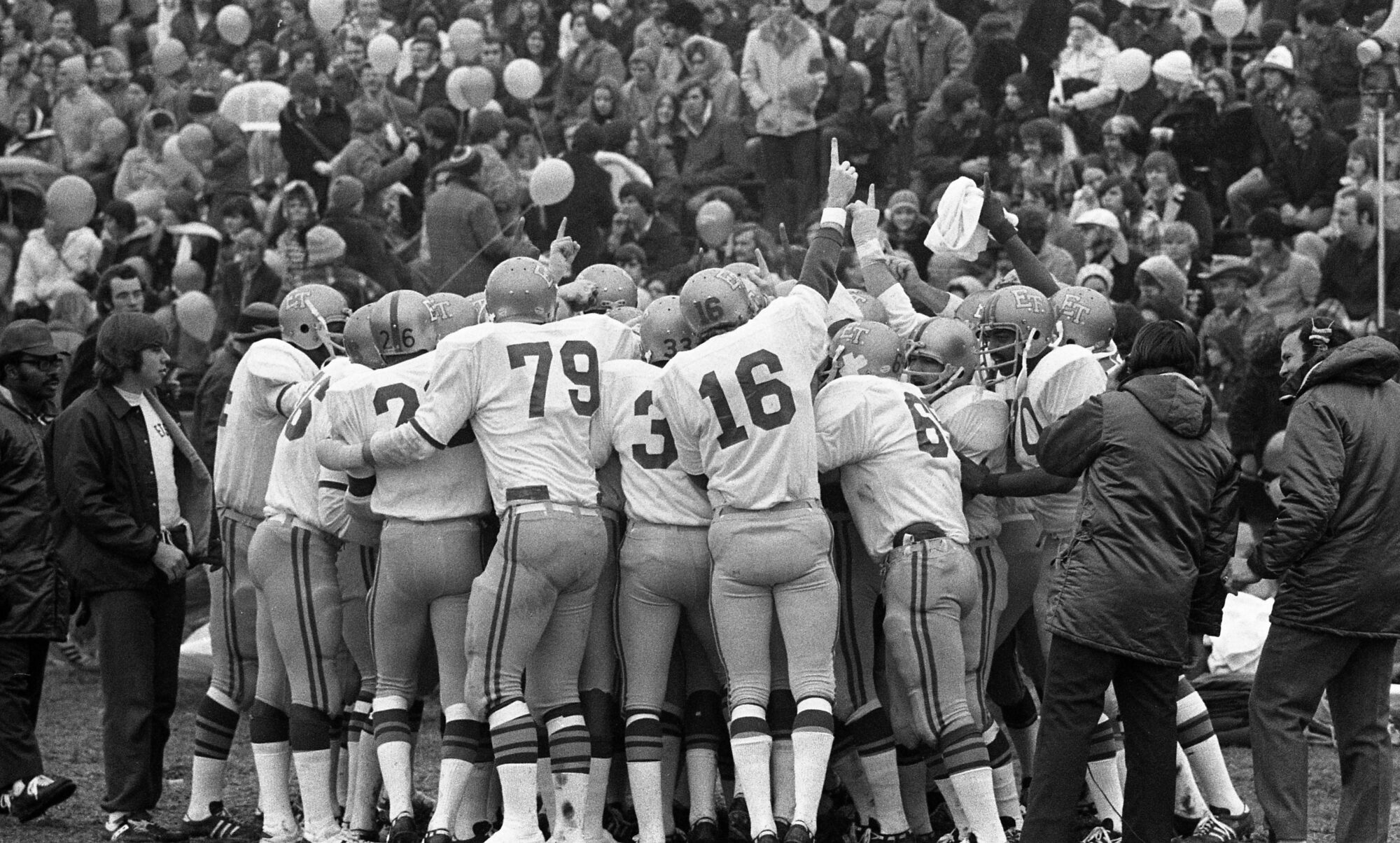 A black and white photo of a group of football players huddling together during a game.
