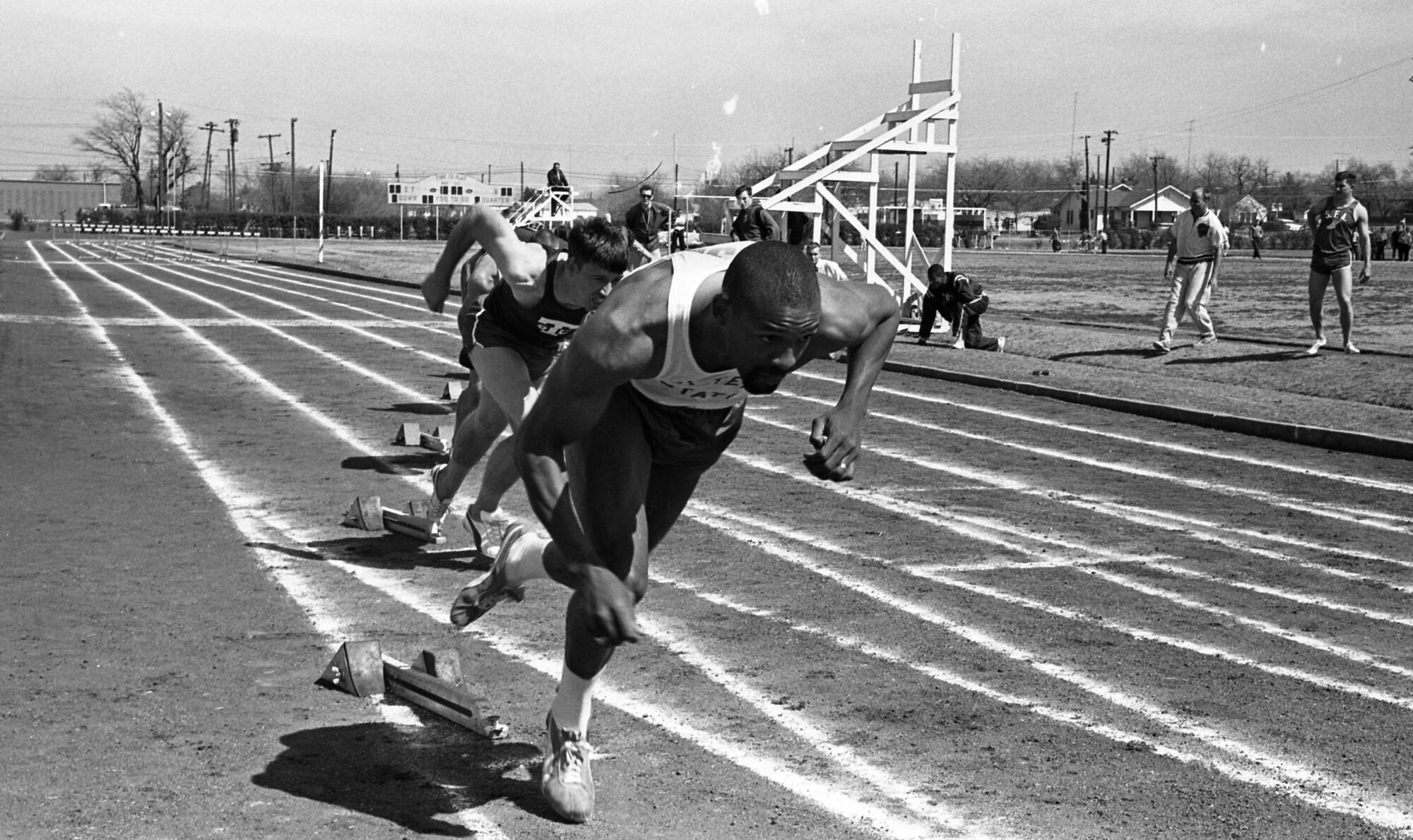 A black and white photo of sprinters racing on a running track.