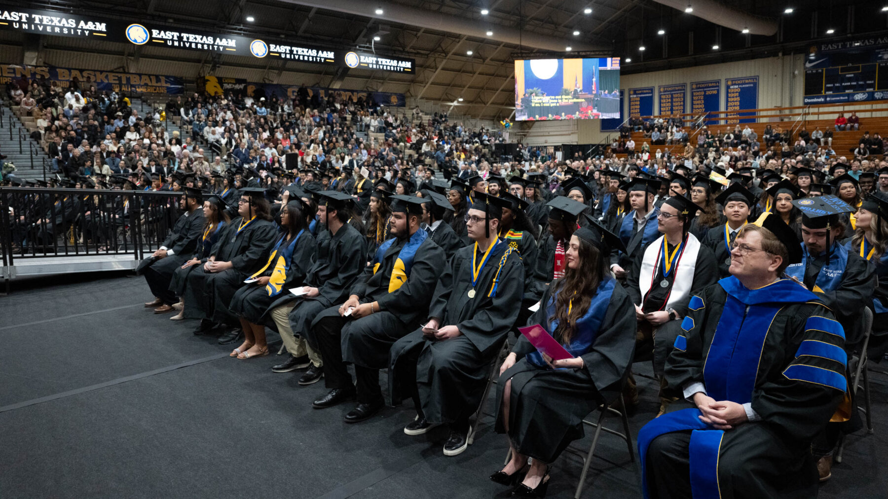 A gymnasium full of college graduates and spectators during a ceremony.