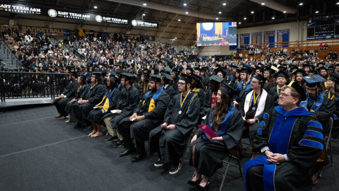 A gymnasium full of college graduates and spectators during a ceremony.