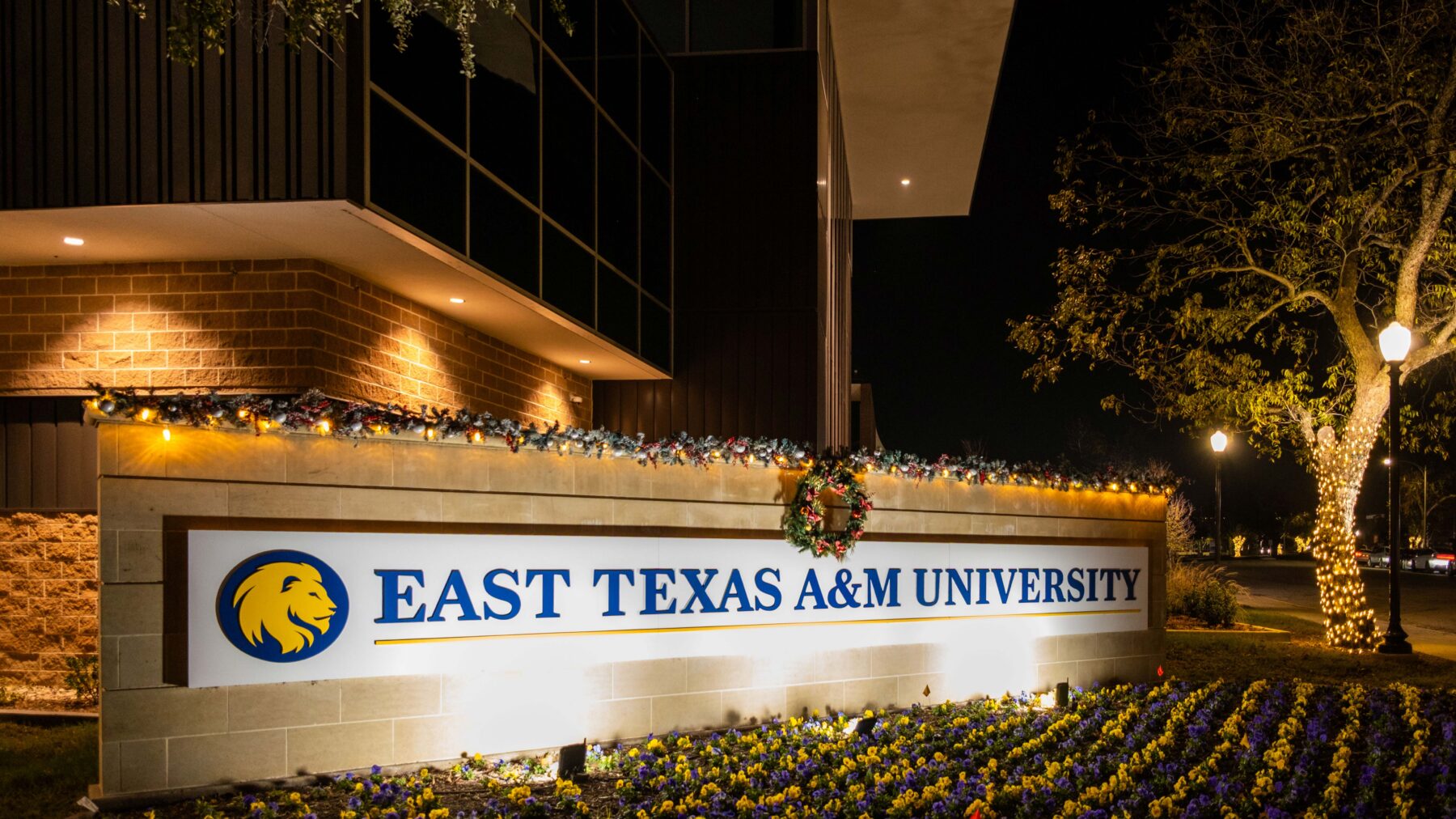 An outdoor sign reading 'East Texas A&M University' lighted with Christmas lights.