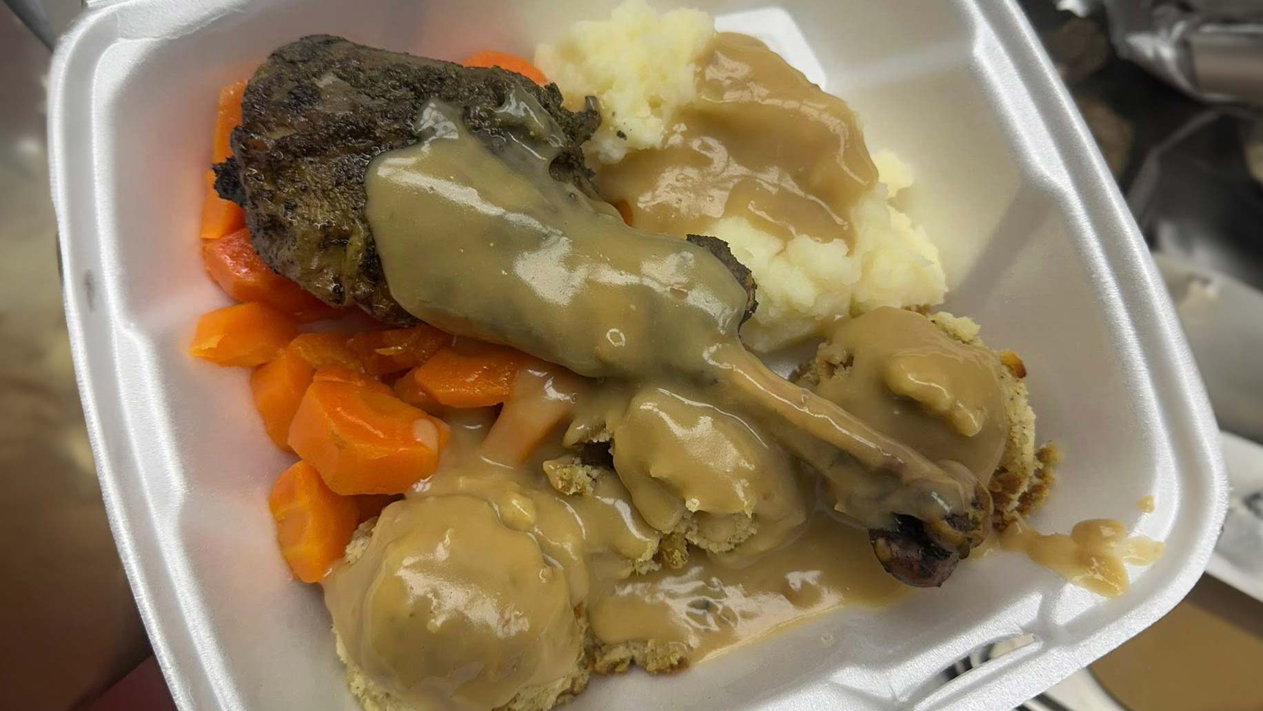 A styrofoam container is filled with food, including carrots, turkey, stuffing, mashed potatoes and gravy.