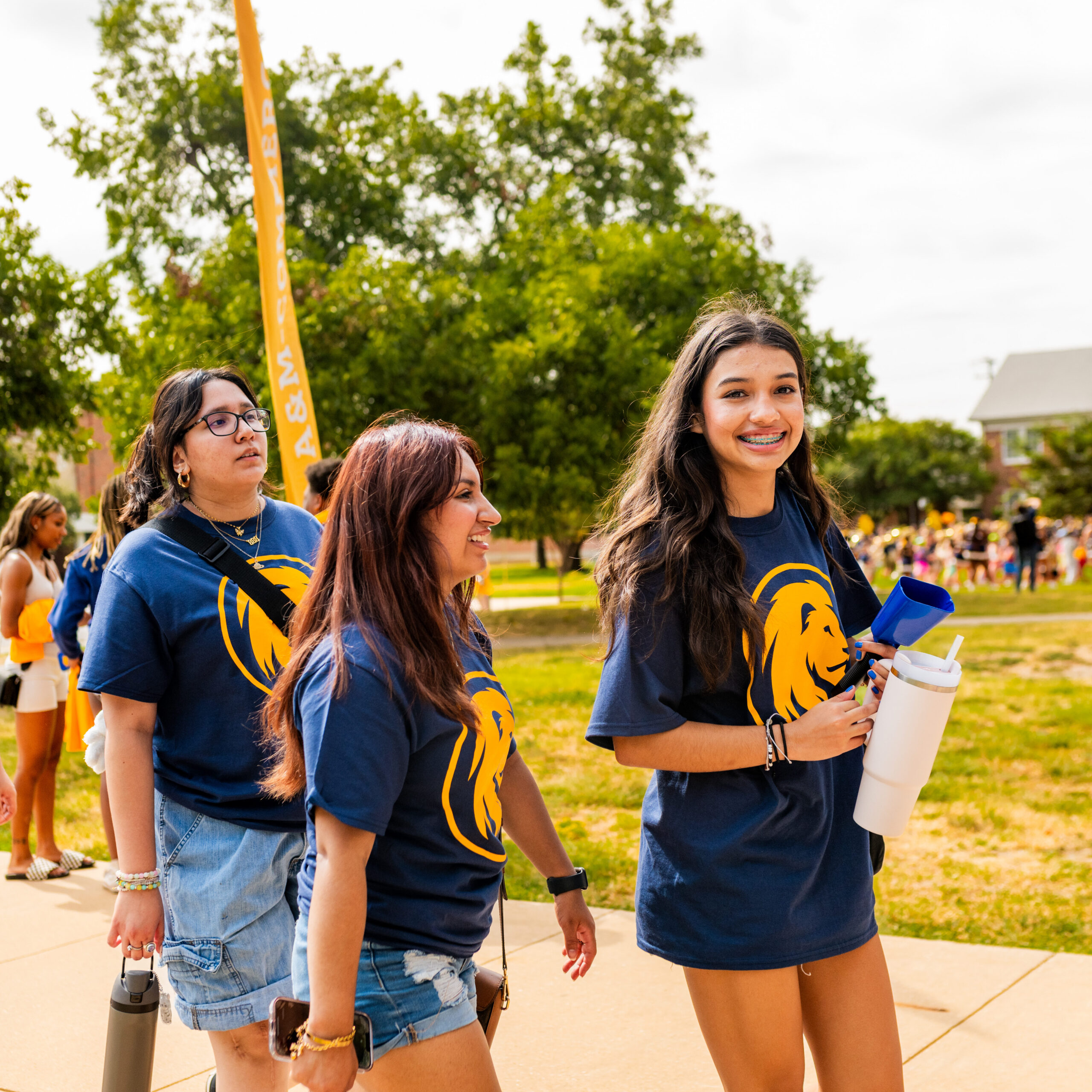 Several students walk together down the sidewalk, wearing blue shirts with a yellow lion head logo on them.