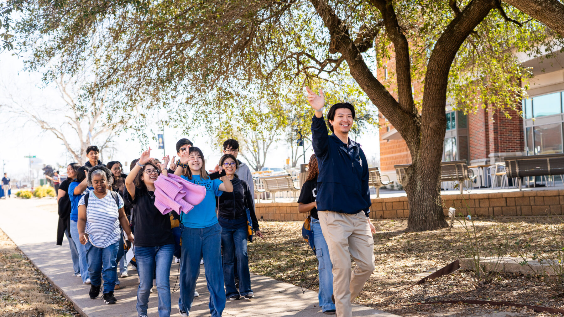 A tour guide leads a group of people down the sidewalk on campus.