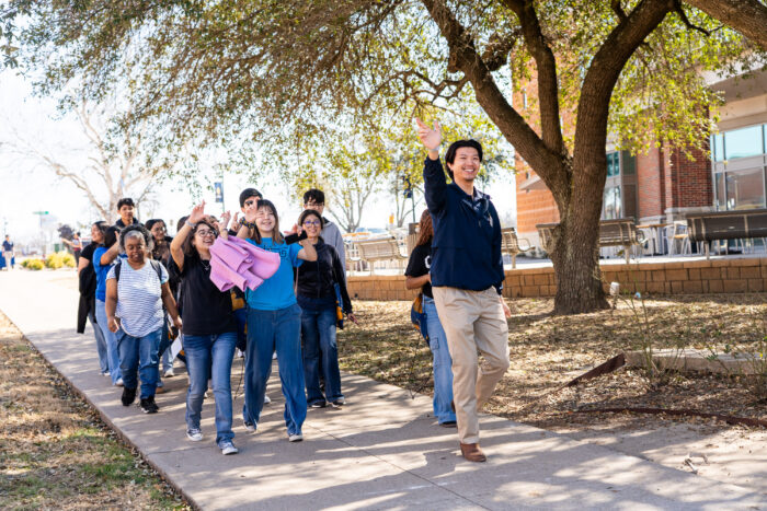 A tour guide leads a group of people down the sidewalk on campus.