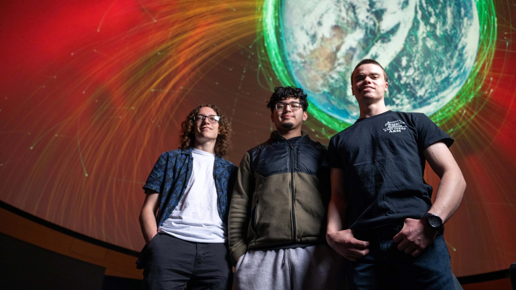 Three young men standing in a row with an image of space and Earth in the background.