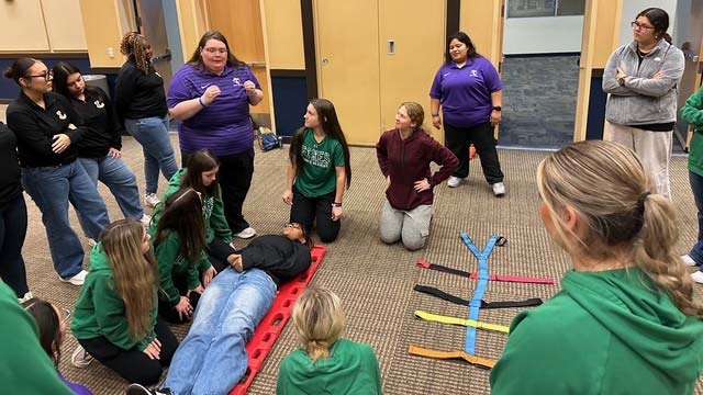 A group of people in an auditorium stand around a person on a spinal board.