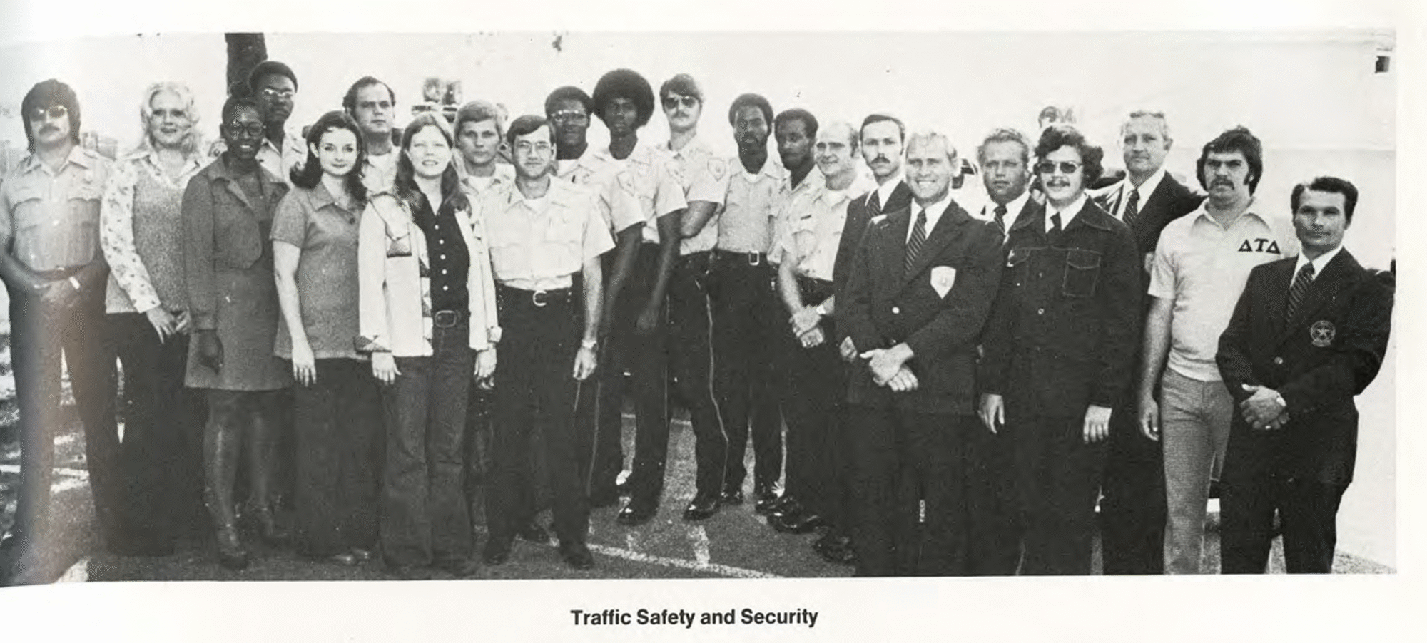 A black and white photo shows a group of people smiling for the camera. There are about 20 people in the photo.