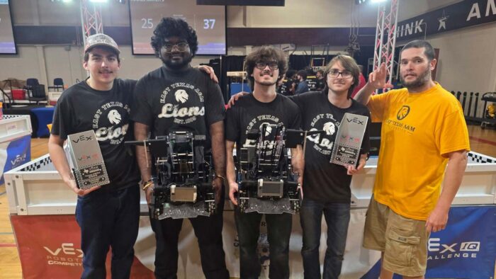 Five men standing in a row, two of whom hold tophies.