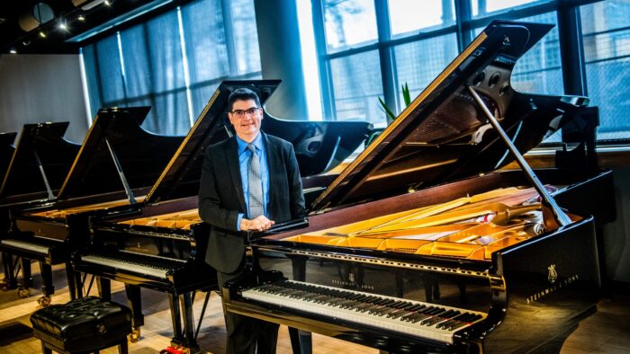 A person in a suit standing near a piano inside of a piano showroom.