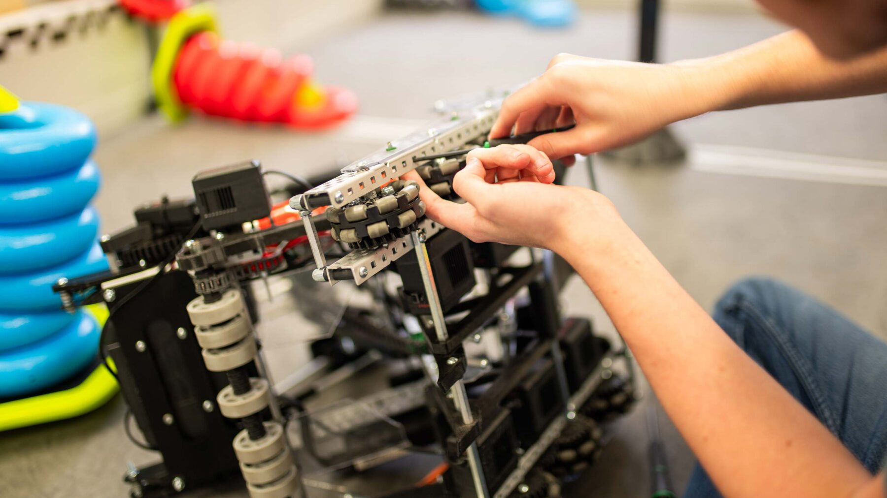 A student's hands working on a wheeled robot.