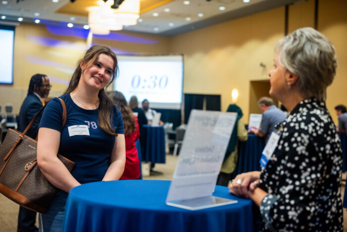 A student smiling in front of a woman talking to her.