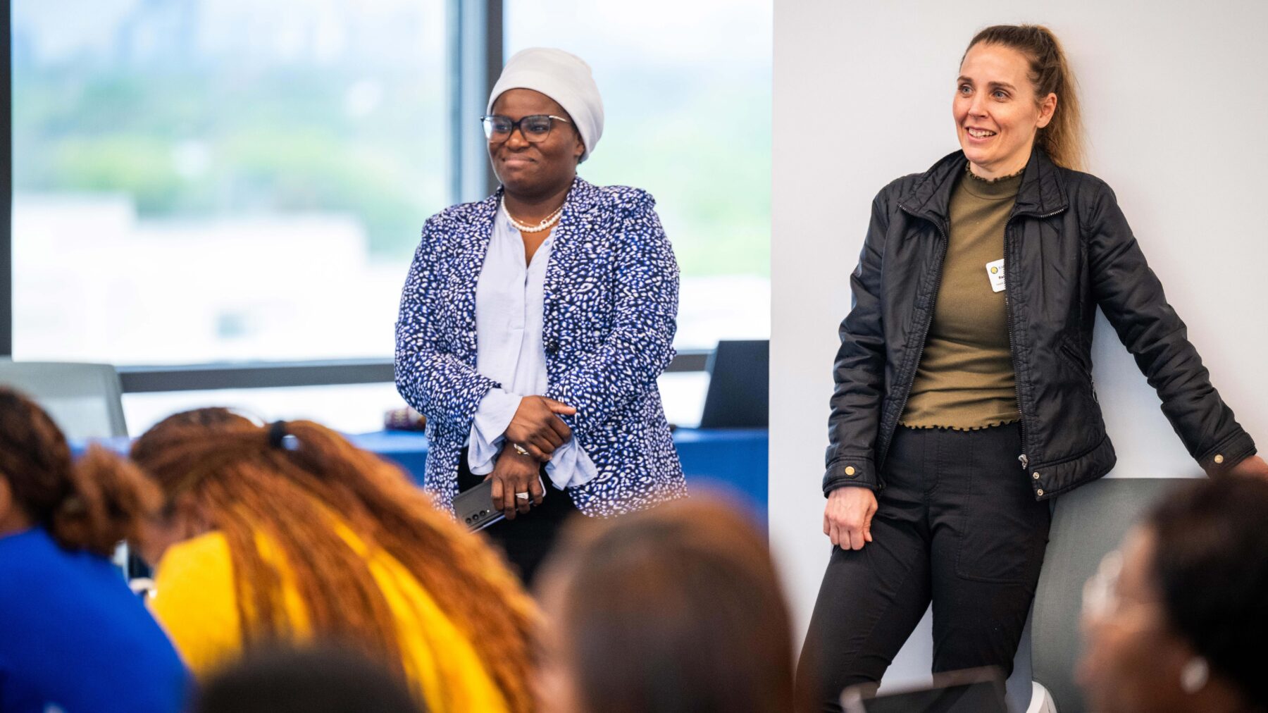 Two women stand smiling near a wall in a classroom.