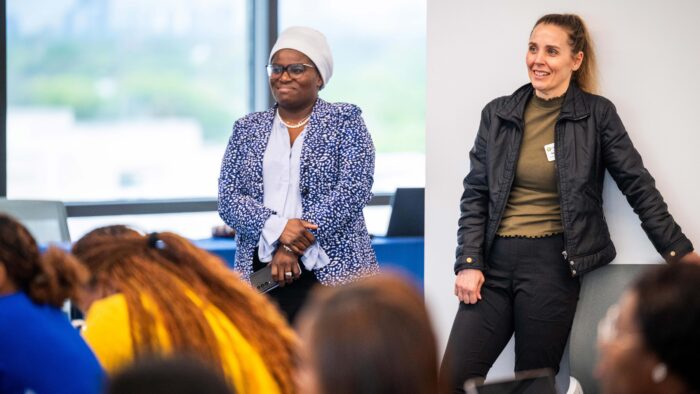 Two women stand smiling near a wall in a classroom.