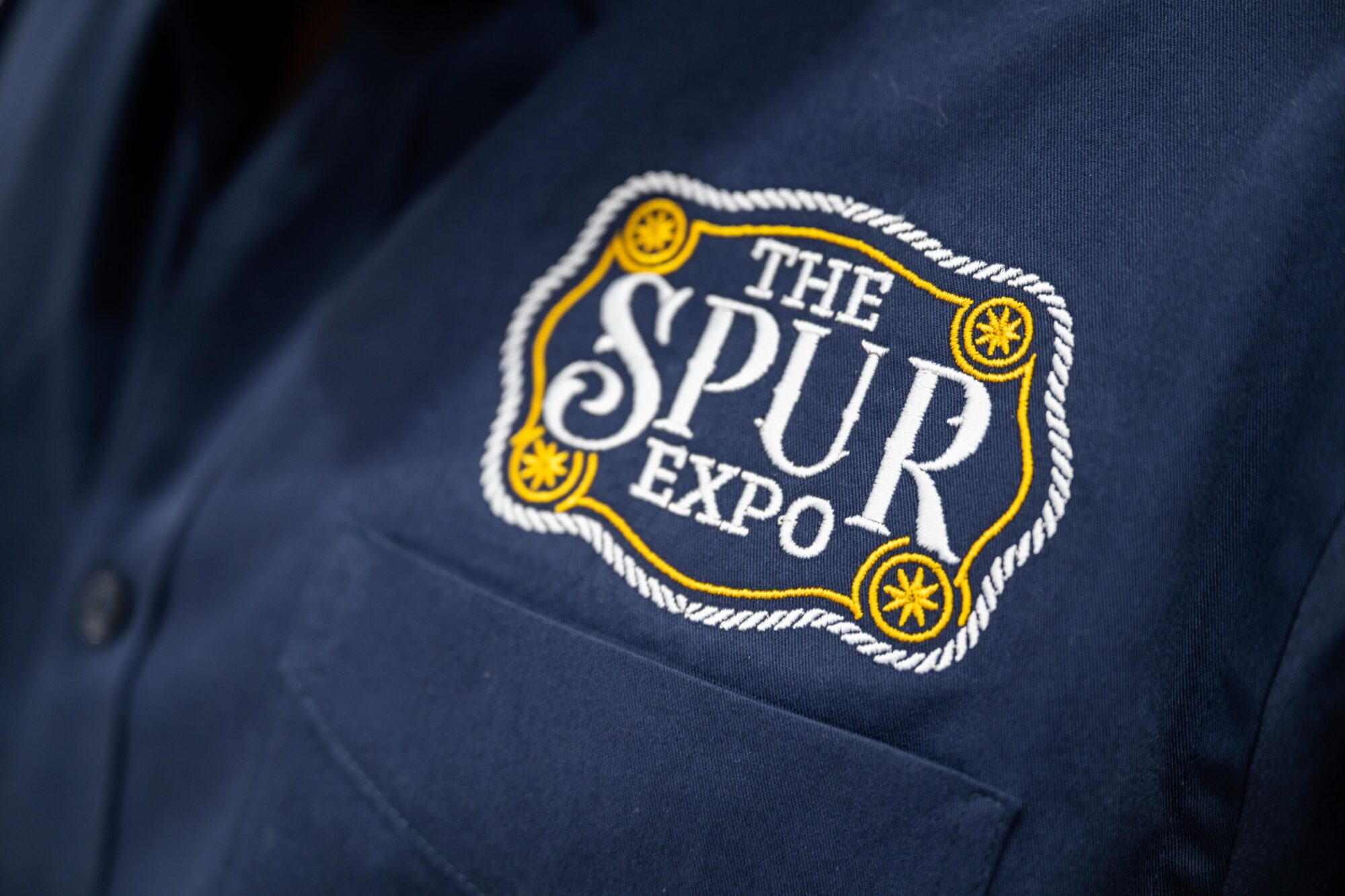 A closeup photo of a blue shirt with the logo for The Spur Expo.