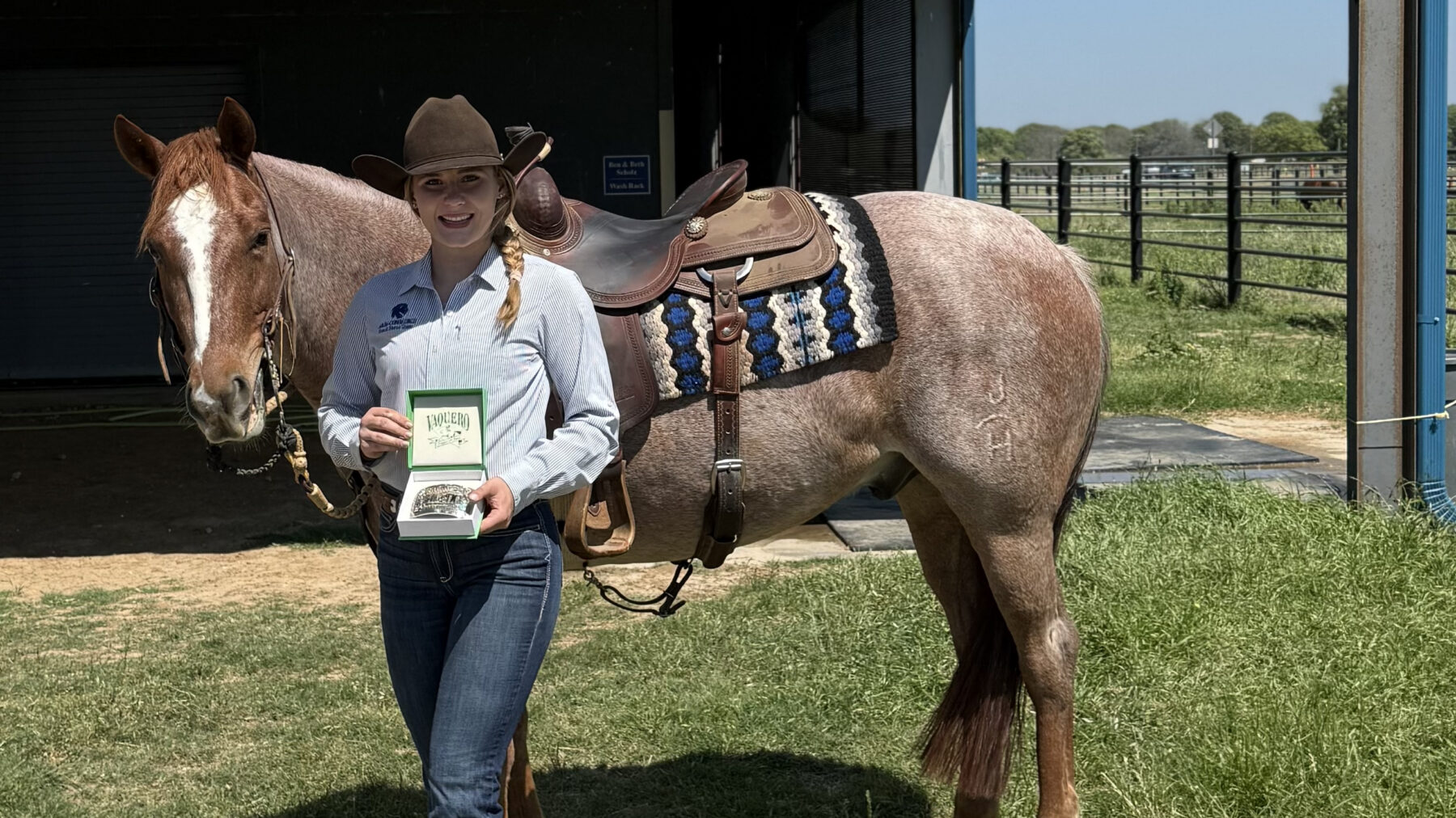 A person in western attire posing with a trophy in front of a horse.