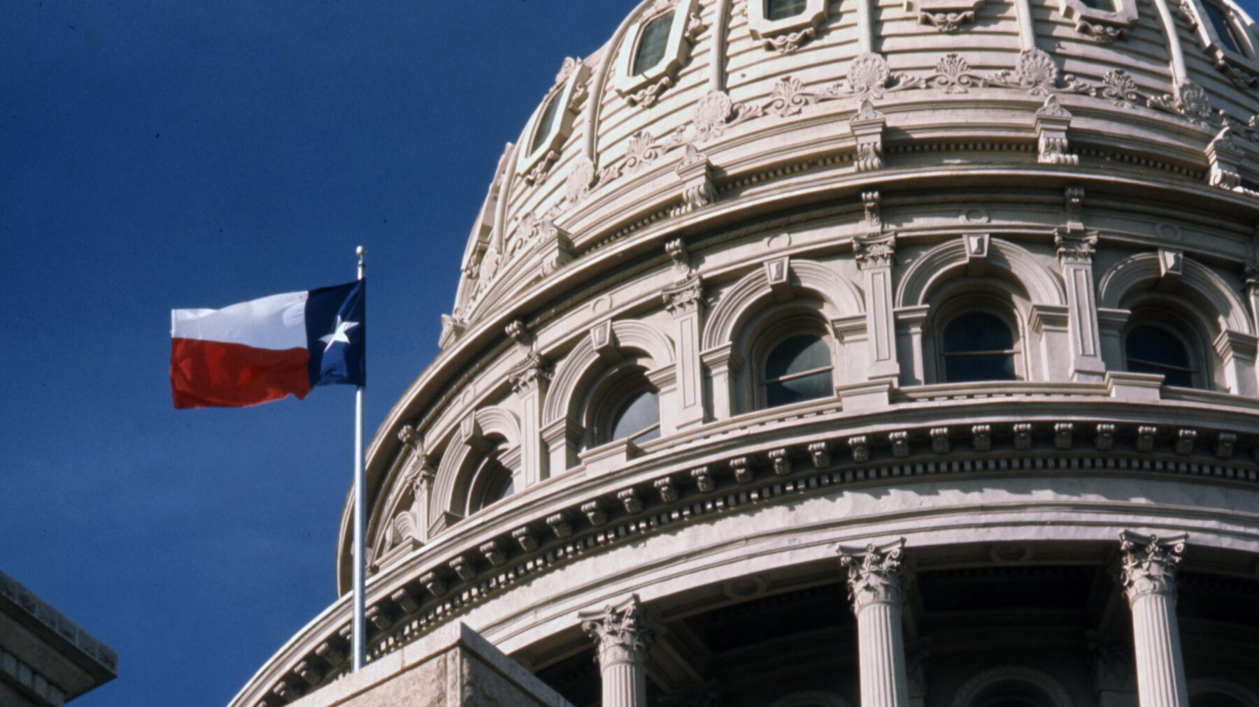 A photo of the Texas state capitol building dome. A Texas flag is visible in the photo.