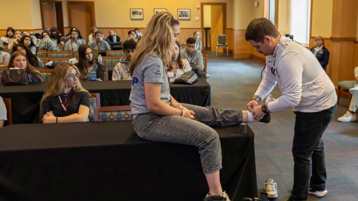Classroom of students, with one girl sitting on a table having her ankle bandaged.