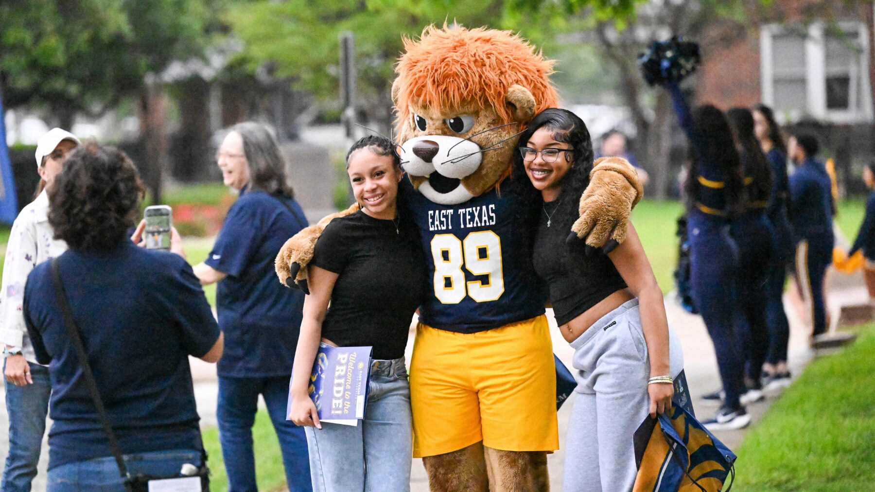 To young women pose with a person in a lion costume.