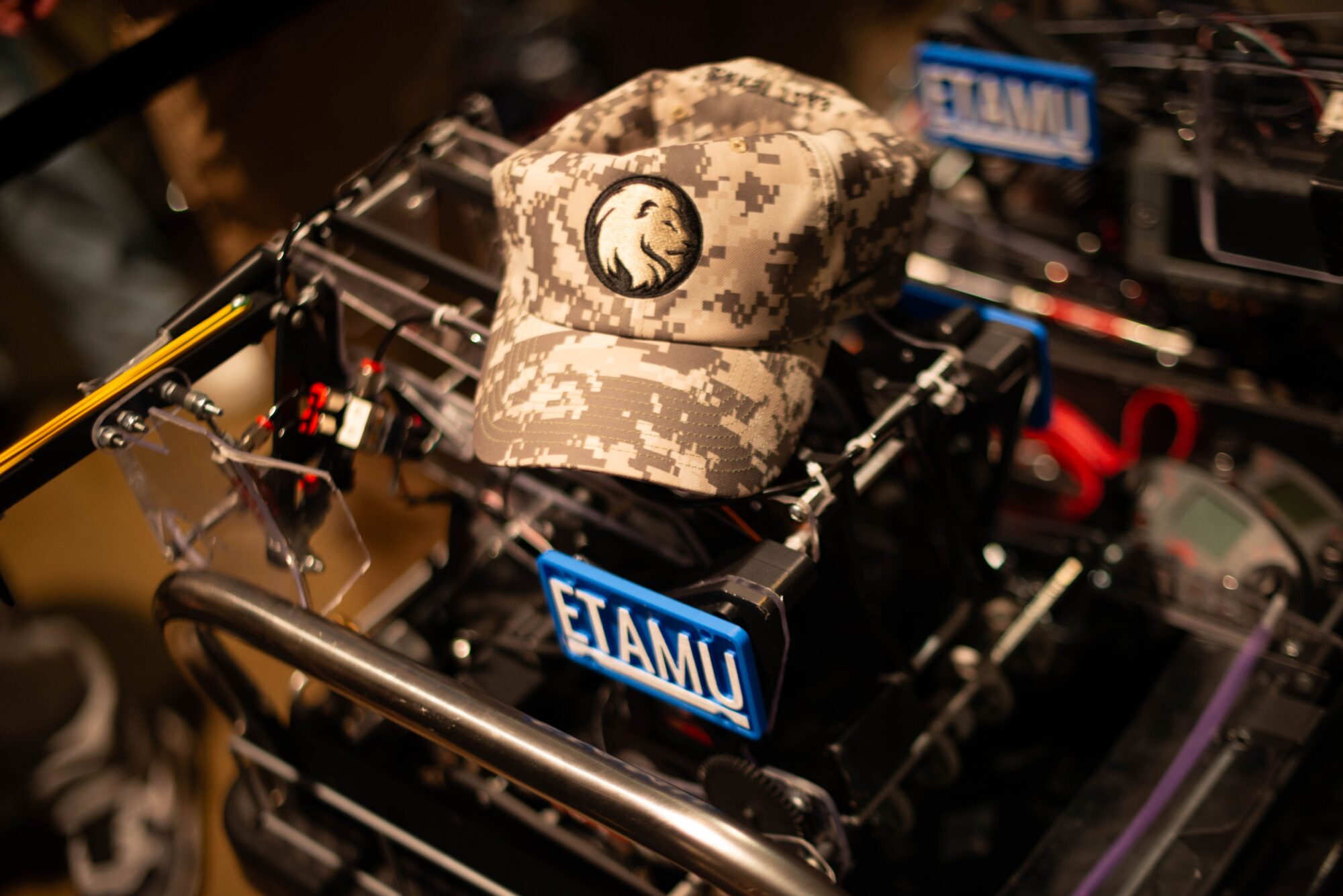 A photo of a baseball cap with a digital camo patter sitting atop a VEX rebot