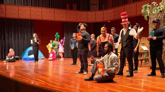 Young people on stage in an auditorium in various costumes.