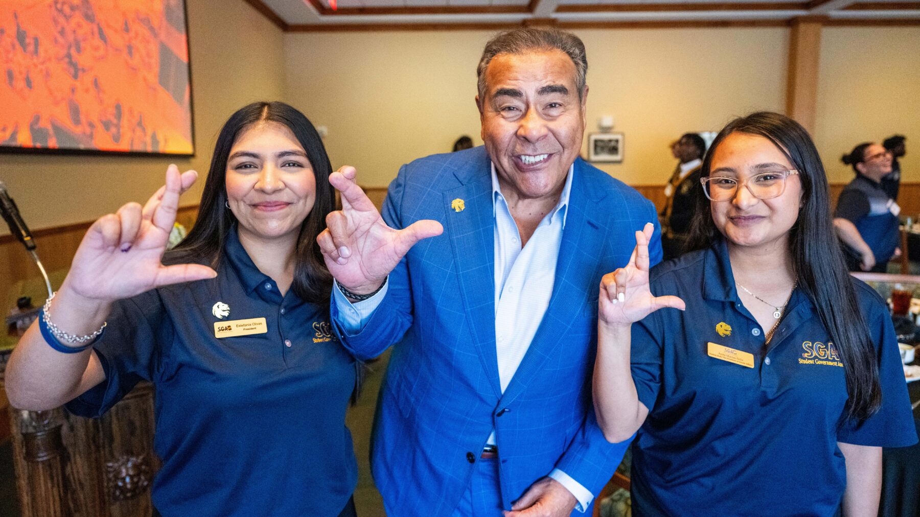 John Quinones stands between two students and makes an "L" with his fingers, the school symbol of East Texas A&M. The two students also make an "L" with their fingers.