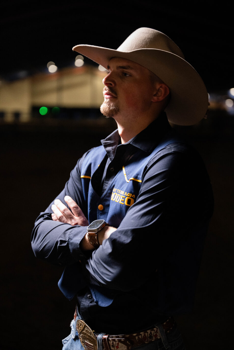 A person in western attire with their arms crossed, looking to the left of the photo.