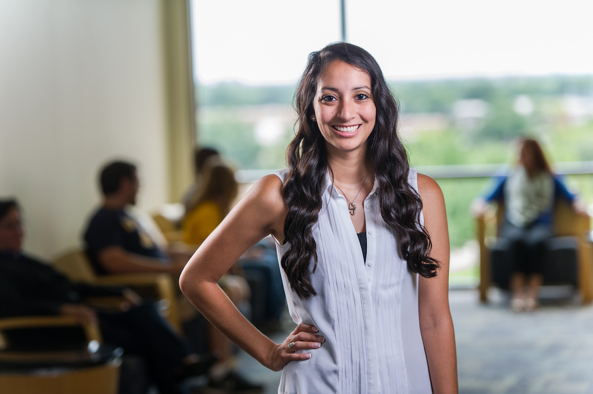 Young professional woman smiling with an office setting behind her.