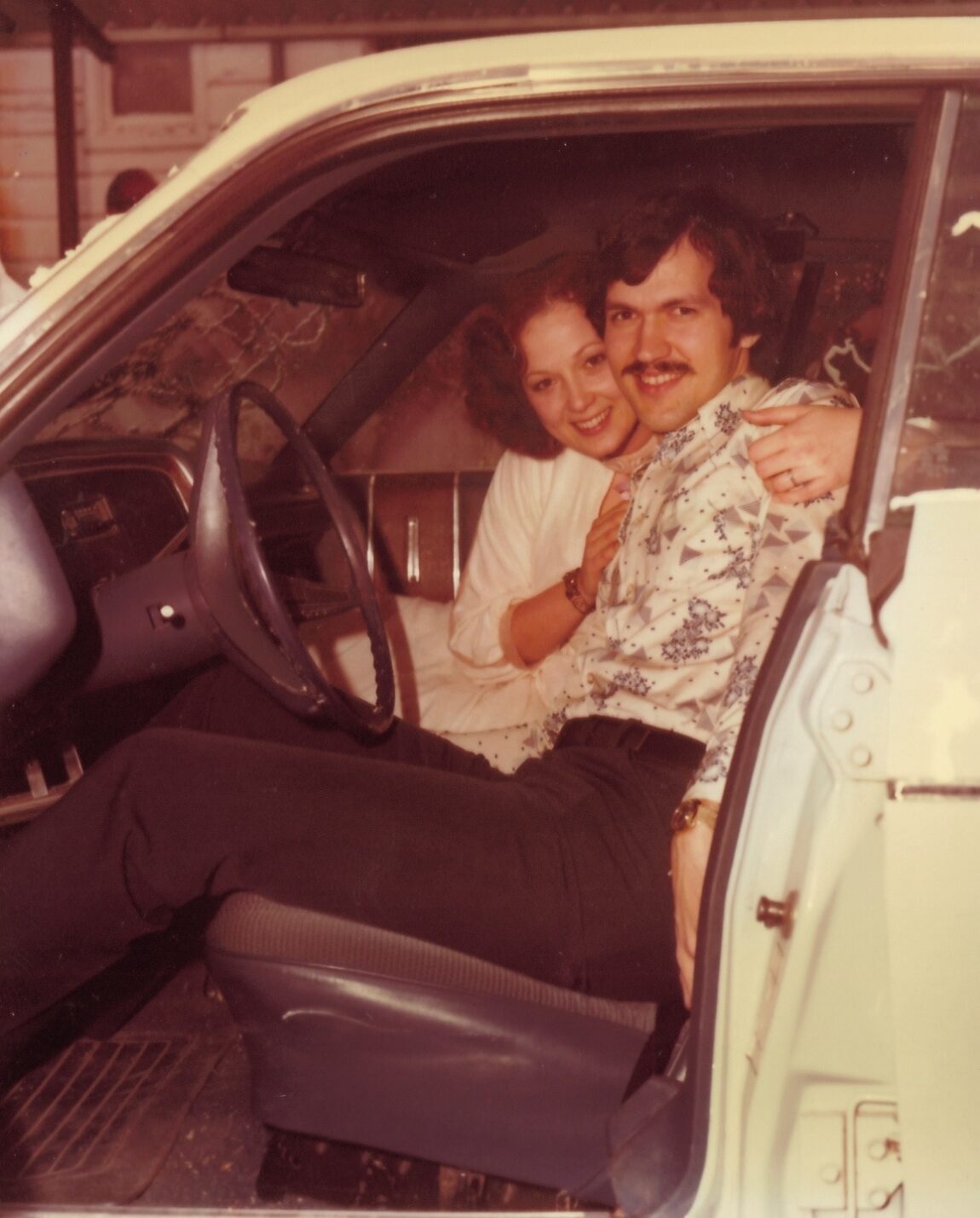 A vintage photo a couple smiling for the camera while seated in a car.