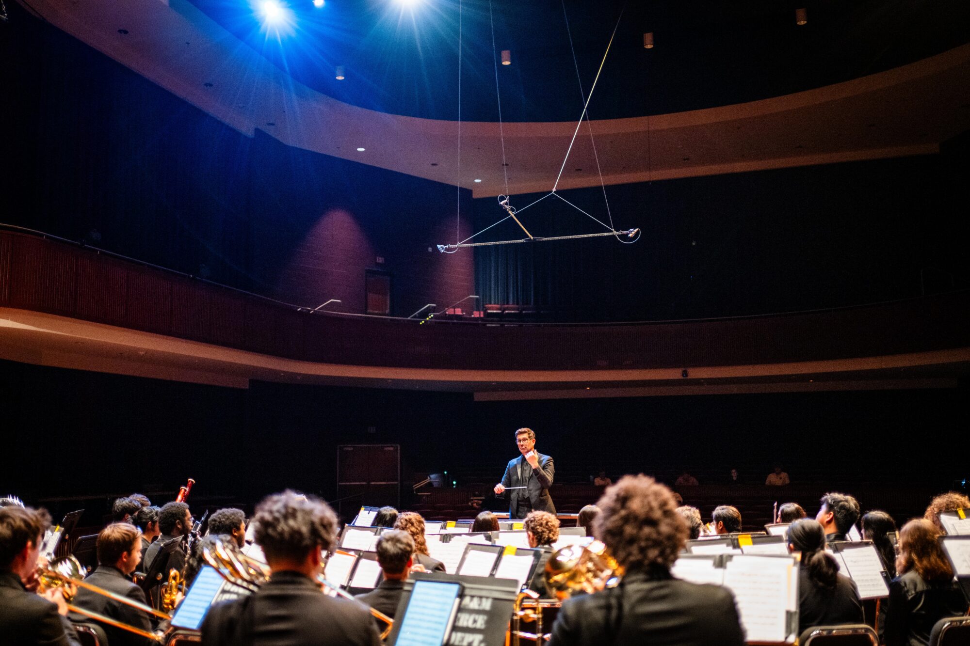 A conductor leading a wind ensemble during a rehearsal in a concert hall.