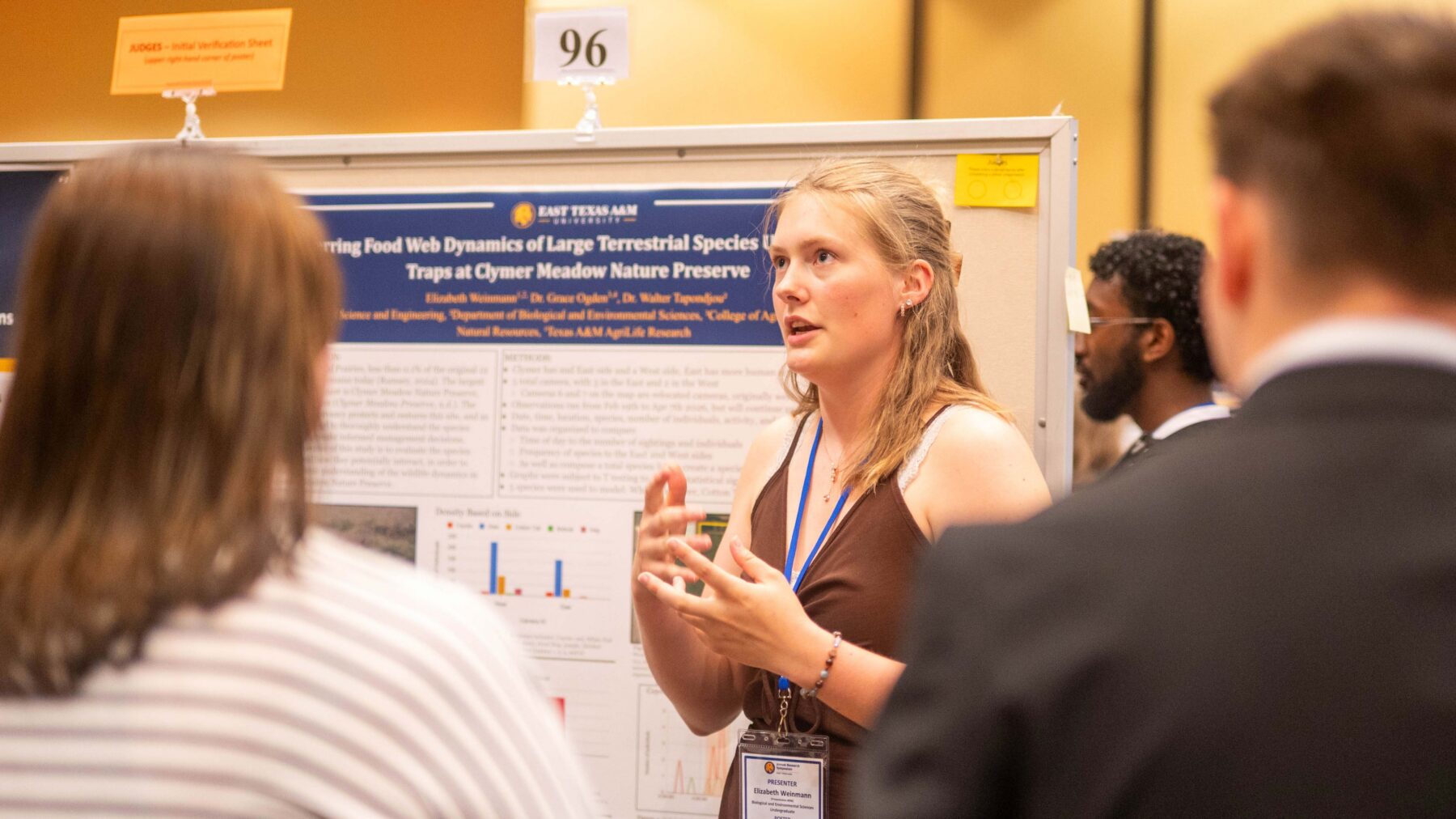 A woman standing in front of a poster display, talking to two other people.