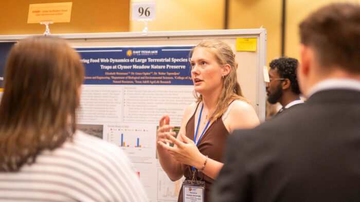 A woman standing in front of a poster display, talking to two other people.