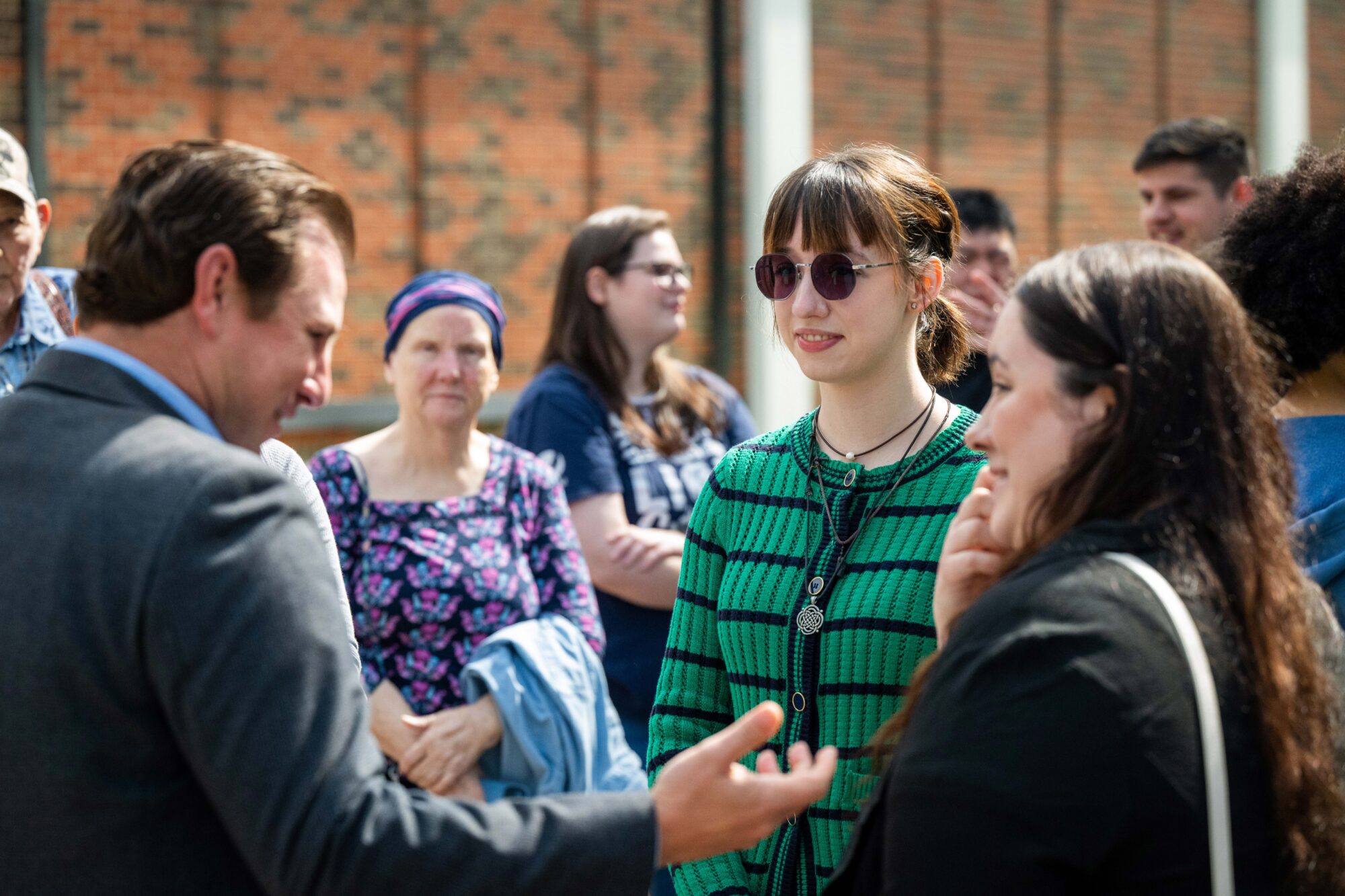 The two artists speak with Devin, a man in a suit. He is smiling at them and his right arm is stretched out, palm up as he speakers. The two artists are smiling.