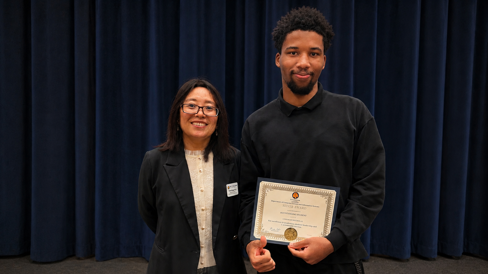 A man and a woman stand side by side holding an award.