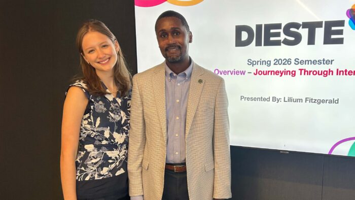 A woman and a man stand side by side in front of a screen that reads Dieste.