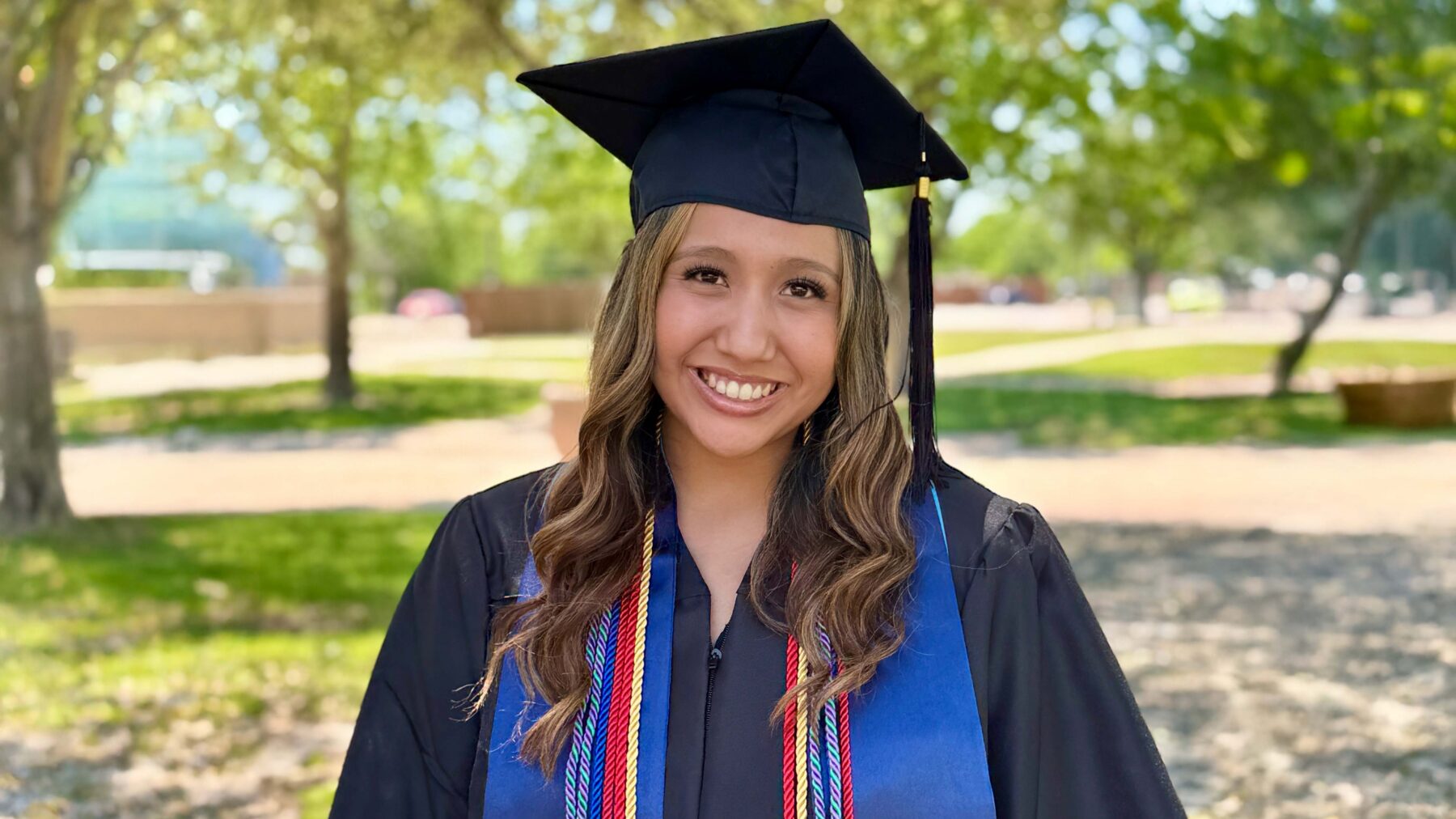 Woman in graduation gown standing outside and smiling.