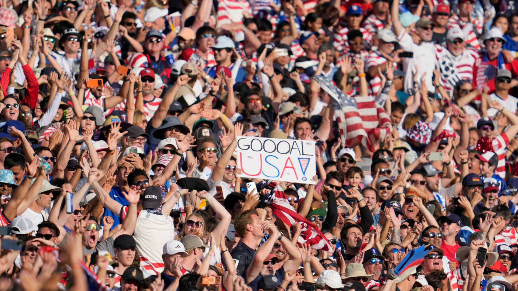 A large number of fans in the crowd of a soccer game. A person is holding a sign the reads "GOOOOAL USA."
